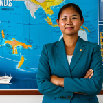마셜 제도 비자 및 입국 절차 - A professional woman in a modest business suit, standing in front of a travel agency poster displayi...